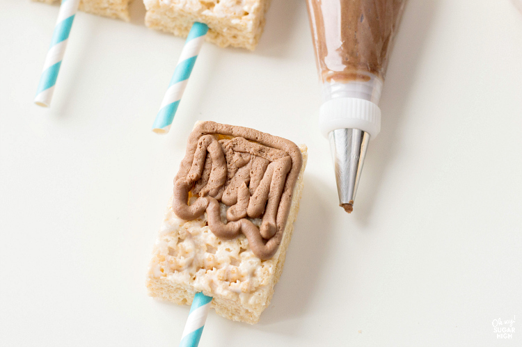 adding chocolate frosting to cereal treats on a stick to make them look like popsicles