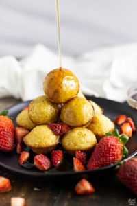 Pouring syrup over pancake muffins with fresh strawberries