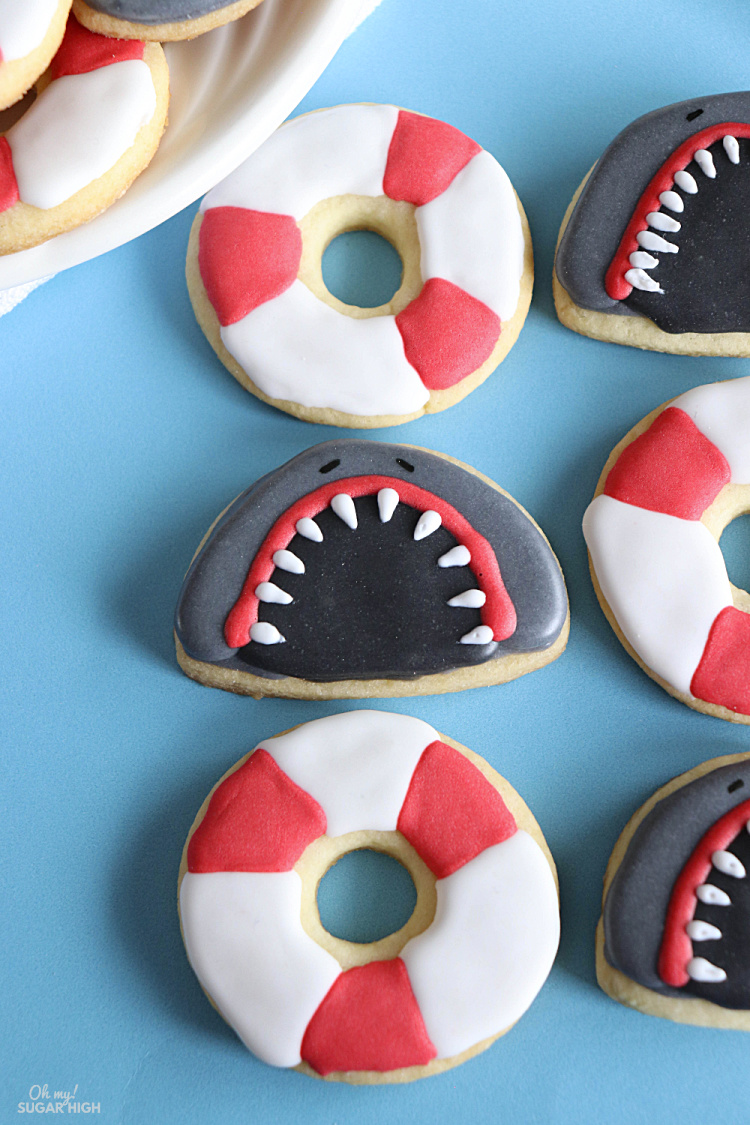 Shark Week Cookies sahen nie besser aus als diese lustigen Haifischzähne und Rettungskekse!  Machen Sie mit dieser Schritt-für-Schritt-Anleitung mit Royal Icing Ihre eigenen Hai-Wochen-dekorierten Kekse.